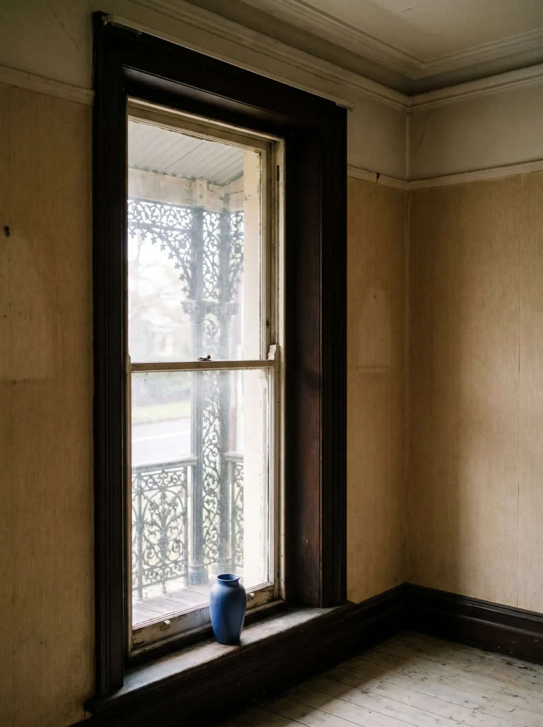 A tall double-hung sash window in a Victorian terrace, iron lacework and the footpath visible just outside